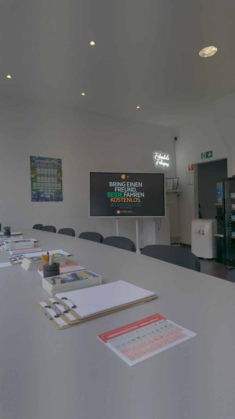 The Fahrschule Fahrspass classroom: a long table with course material, chairs, and a screen on the end wall