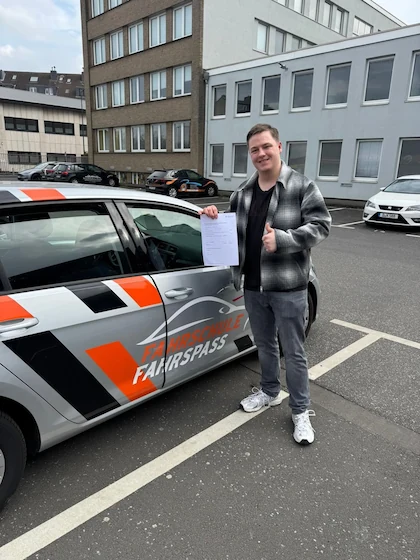 Bestanden — Schülerin oder Schüler mit dem Führerschein vor dem Fahrschulwagen