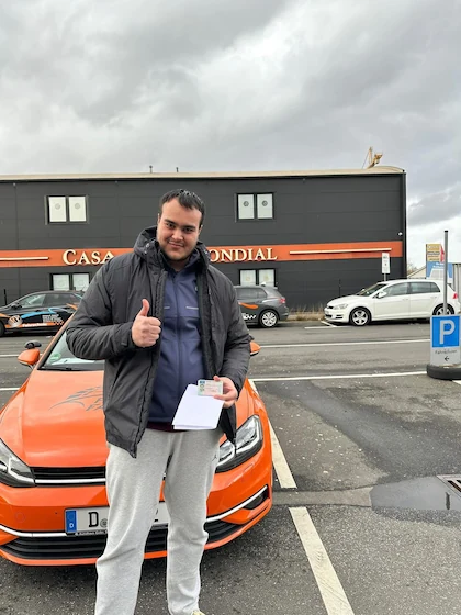 Bestanden — Schülerin oder Schüler mit dem Führerschein vor dem Fahrschulwagen