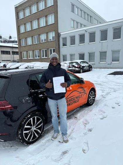 Bestanden — Schülerin oder Schüler mit dem Führerschein vor dem Fahrschulwagen