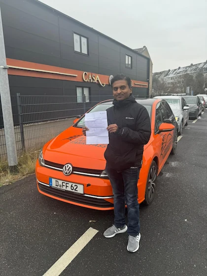 Bestanden — Schülerin oder Schüler mit dem Führerschein vor dem Fahrschulwagen